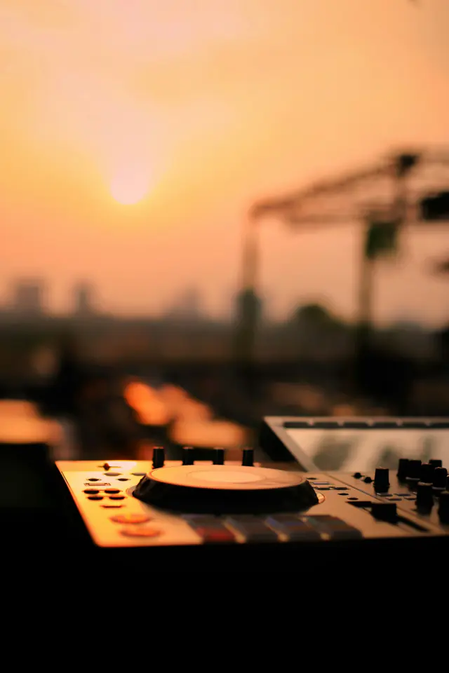DJ mixer and decks set up on a rooftop against a hazy sunset skyline