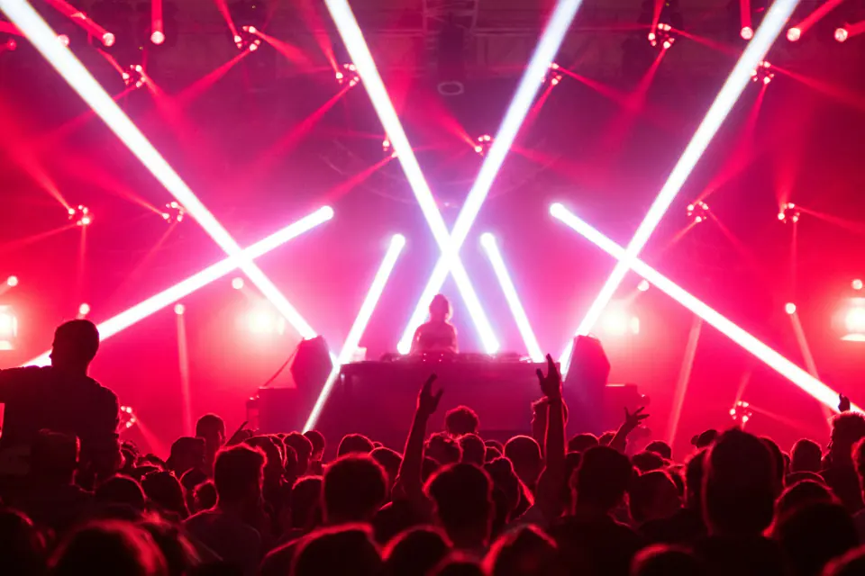 Crowd with hands up under red laser beams in front of a DJ stage