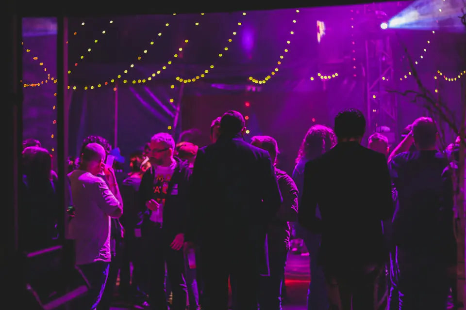 Guests mingling and dancing under purple lights and string lights at an evening party