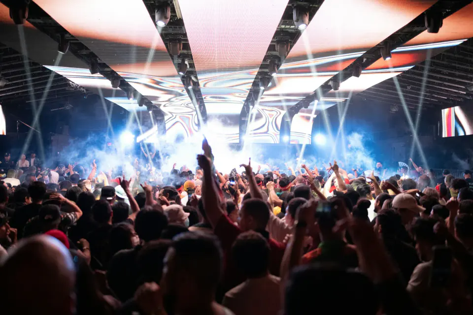Huge festival crowd with hands raised beneath a bright stage lighting rig