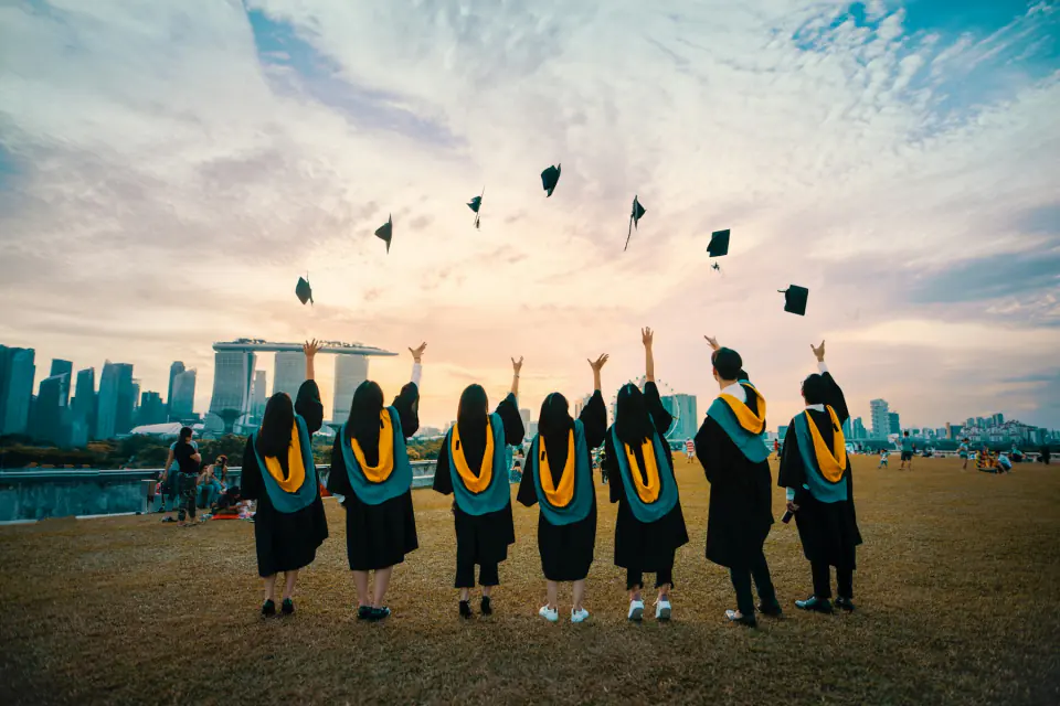Graduates seen from behind tossing their caps into a sunset sky