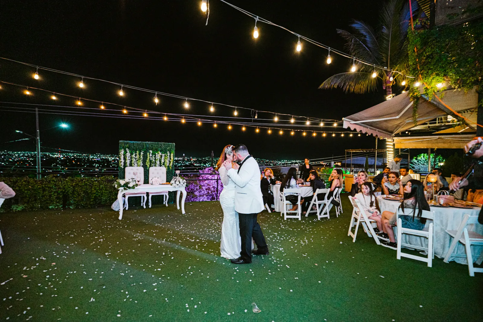 Newlyweds sharing their first dance on a lawn under strings of café lights