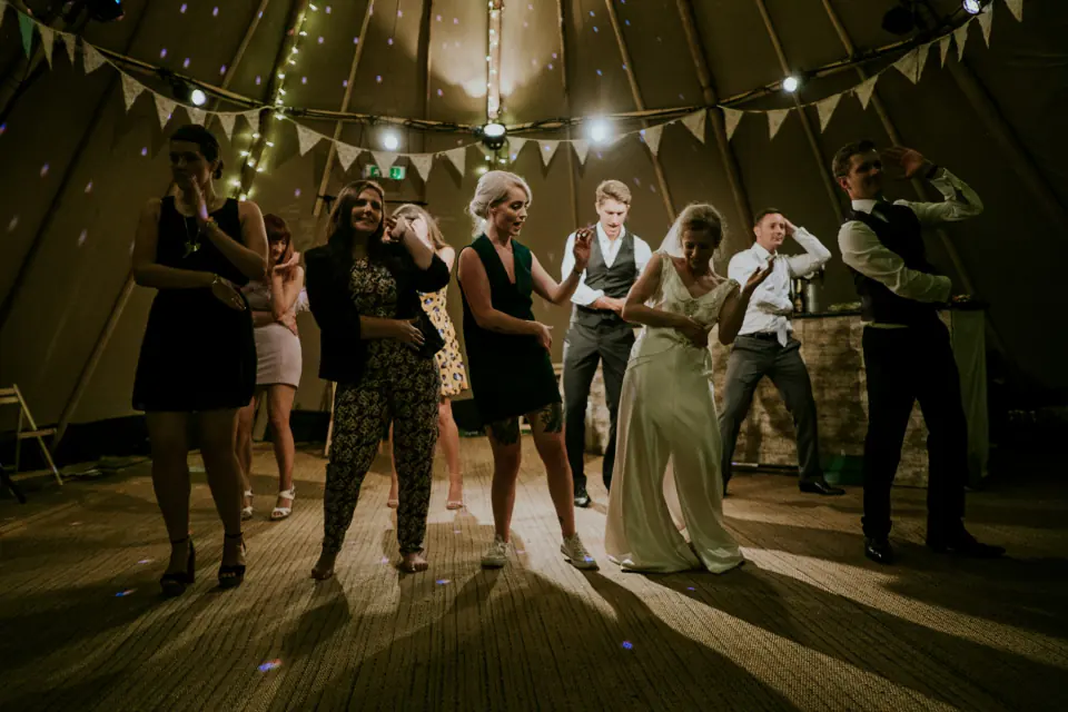 Wedding guests dancing in a rustic barn under strings of lights